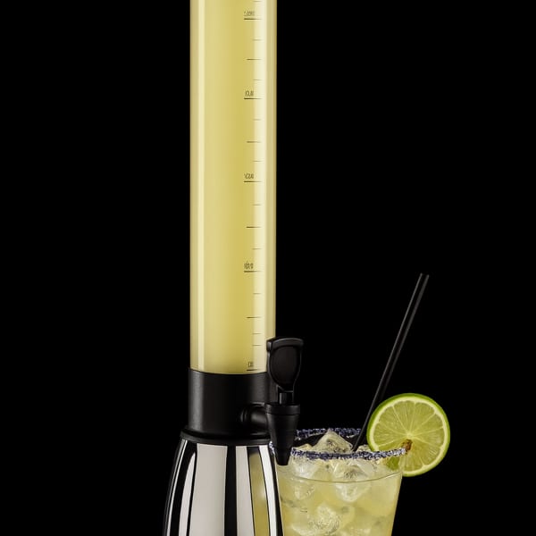 A tall drink dispenser filled with yellow liquid next to a margarita with a lime slice.