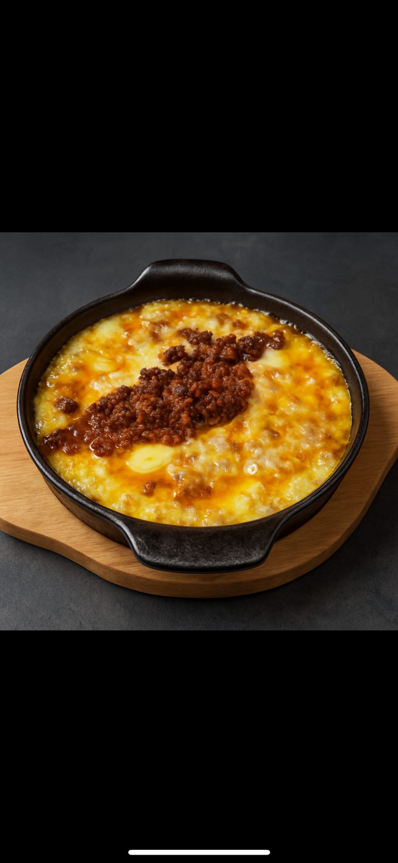 A cast iron skillet of bubbling queso fundido with chorizo, on a wooden board.