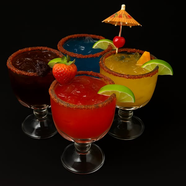 Four colorful frozen drinks with chili-lime rims, garnished with fruit and a tiny umbrella.