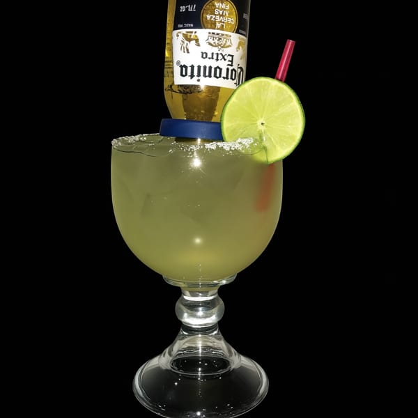 A Coronita margarita with a lime wedge and red straw in a large stemmed glass.