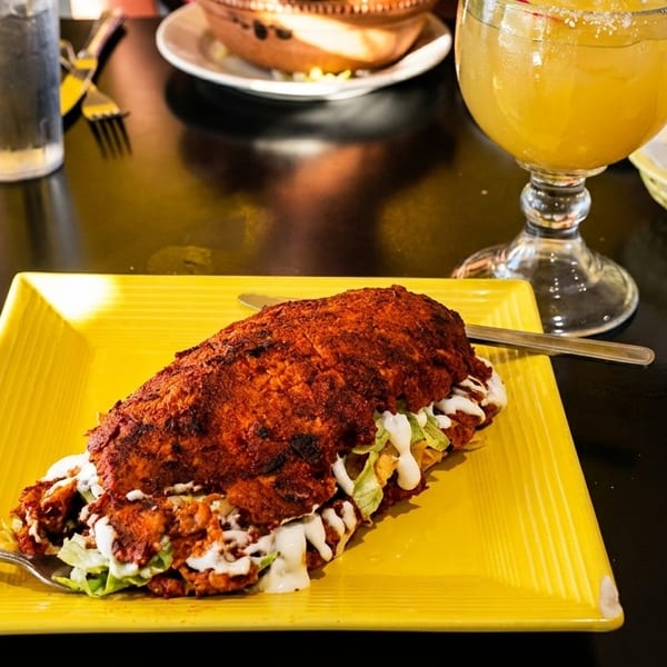 A large, crispy, red-brown Mexican torta sandwich on a yellow plate with lettuce and crema.