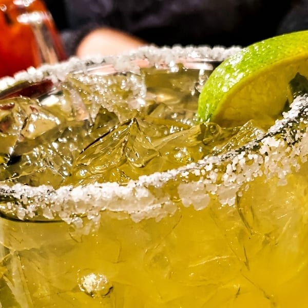 Close-up of a vibrant green margarita with a salted rim, ice, and a lime wedge.