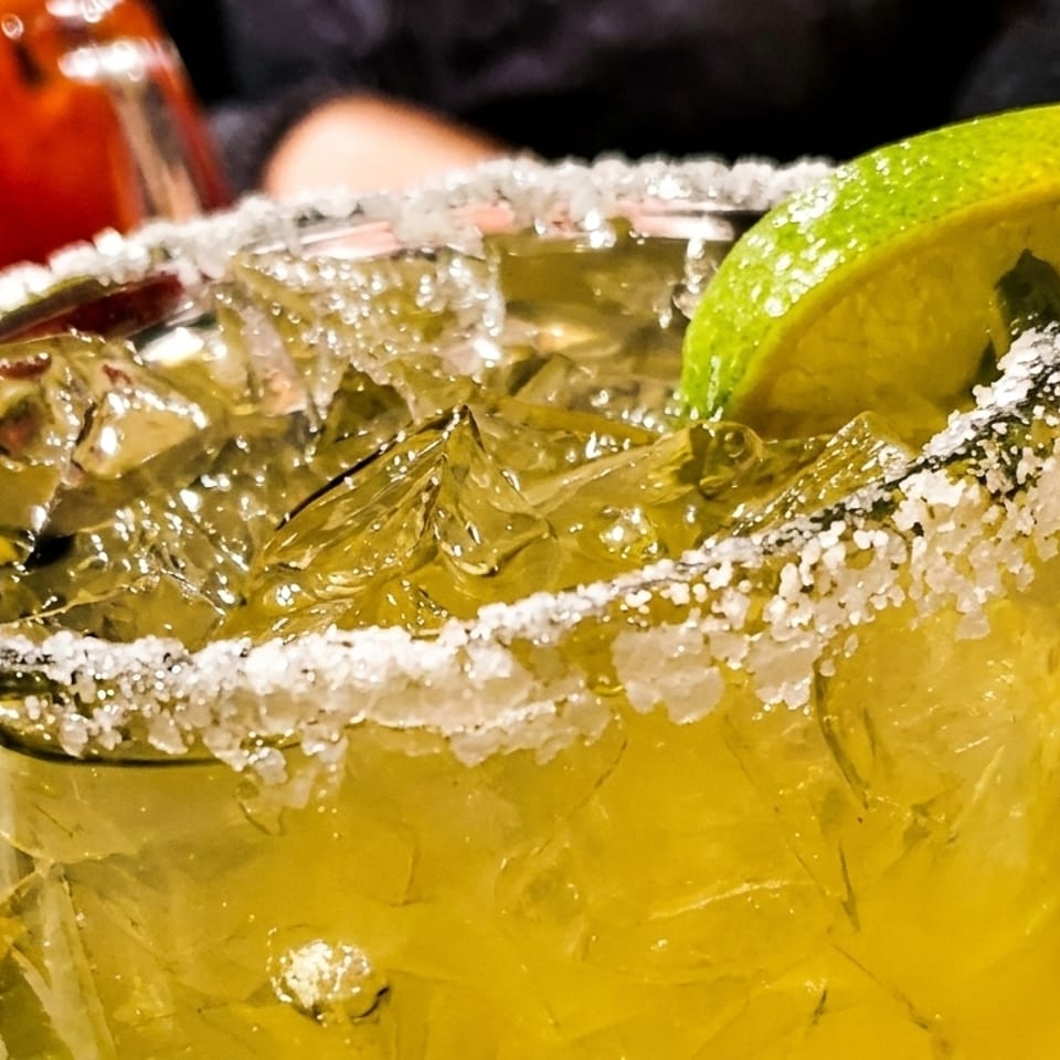 Close-up of a vibrant green margarita with a salted rim, ice, and a lime wedge.