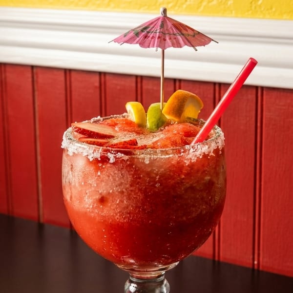 Strawberry margarita with a salted rim, fruit garnishes, a red straw, and a pink umbrella.