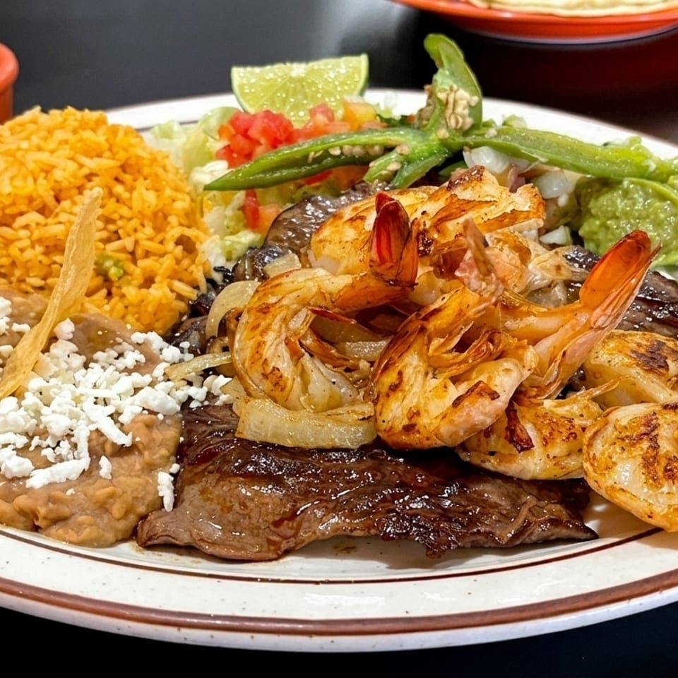 A Mexican surf and turf plate with grilled shrimp, steak, rice, refried beans, guacamole, and salsa.